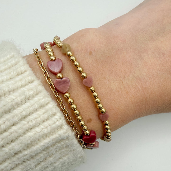 Bracelet with pink heart-shaped beads and gold chain on a wrist against a white background