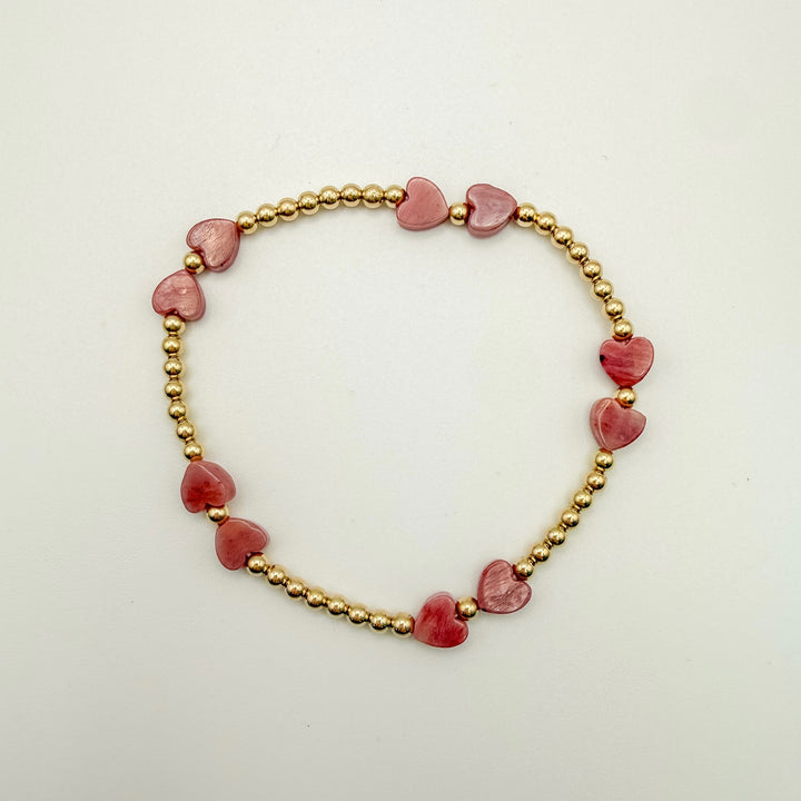 Bracelet with pink heart-shaped beads and gold beads on a light background