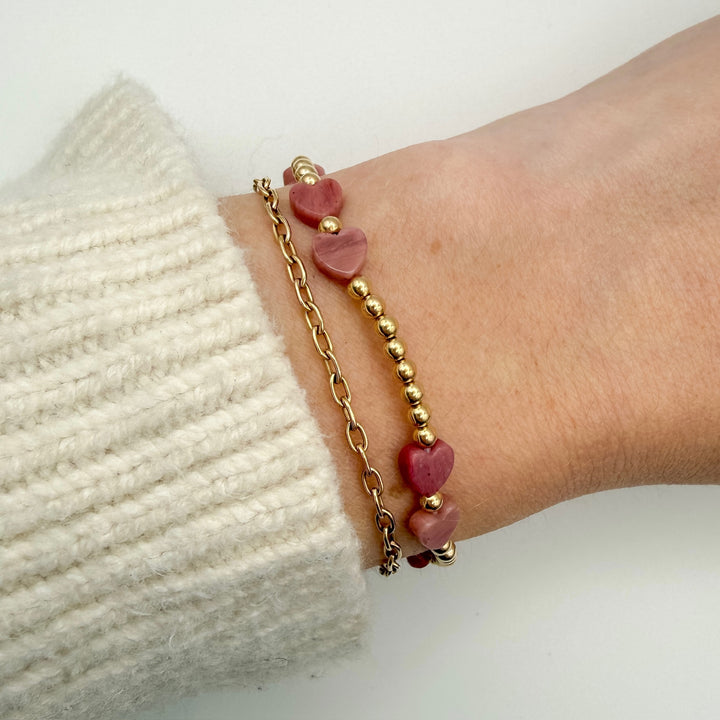Bracelet with pink heart-shaped beads and gold chain on wrist against a white background
