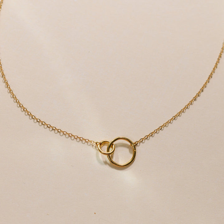 Gold necklace with a small round pendant on a beige background